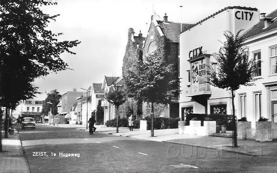 Centrum Zeist0010, 1e Hogeweg. 1962.jpg - De 1e Hogeweg in 1962. Gezicht op  witte pand van Guco,(Pension Boschzicht) daarnaast het Citytheater en in Juni 1993 werd de bioscoop gesloopt en in Januari 1994 ging het voormalige pension tegen de grond. En op de plek van het schoolgebouw stond is nu V&D gevestigd op deze plek. Einde van de straat is Modezaak Duetz te zien.